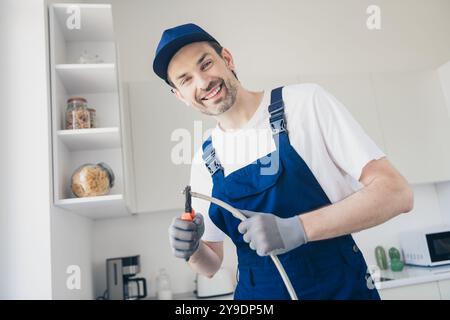 Bricoleur souriant dans une cuisine moderne travaillant sur l'installation d'appareils avec des outils professionnels et une expertise Banque D'Images