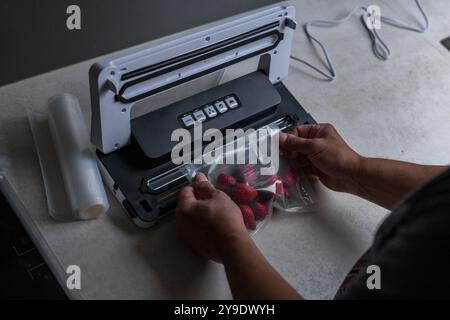 la main d'un homme utilise une machine à vide pour emballer les fraises sous vide dans des sacs en plastique. . Photo de haute qualité Banque D'Images