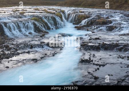 Une belle cascade en cascade coule sur un terrain rocheux, avec de l'eau bleue claire qui coule doucement à travers le paysage, créant un calme et nature Banque D'Images