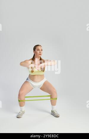 Une femme concentrée dans un crop top effectue un squat de bande de résistance, montrant la force et la détermination. Banque D'Images