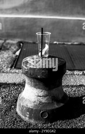 Tasse en plastique abandonnée avec de la paille noire sur une borne de circulation avec une tranche d'orange et un Spritz dans une rue italienne à Ferrare Banque D'Images