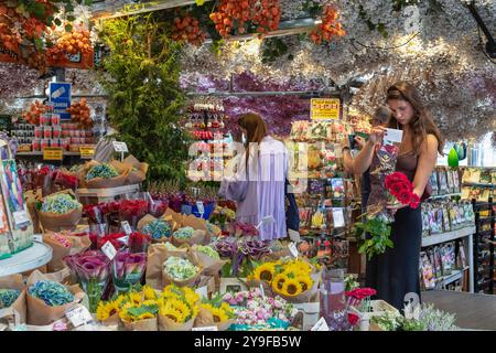 Les touristes regardent les fleurs dans un étal de fleurs au marché flottant aux fleurs à Amsterdam. Banque D'Images