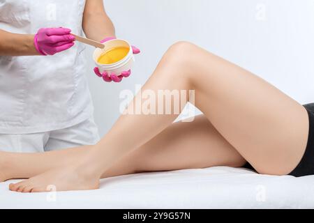 Une esthéticienne fait une épilation en pâte de sucre des jambes d'une femme dans un salon de beauté. Cosmétologie esthétique féminine. Banque D'Images