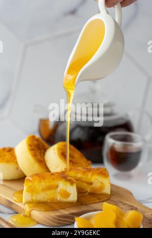 Miel doré versé sur des mini cheesecakes garnis de pêche servis sur une planche de bois avec une tasse de thé chaud. Banque D'Images