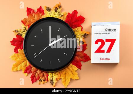 Bavière, Allemagne - 10 octobre 2024 : passage à l'heure d'hiver le 27 octobre, représenté par une grande horloge noire et une page de calendrier. L'horloge symbolise la réinitialisation d'une heure. Des feuilles d'automne colorées entourent l'horloge *** Zeitumstellung auf Winterzeit am 27. Oktober, dargestellt durch eine große schwarze Uhr und ein Kalenderblatt. Die Uhr symbolisiert die Rückstellung um eine Stunde. Bunte Herbstblätter umgeben die Uhr Banque D'Images