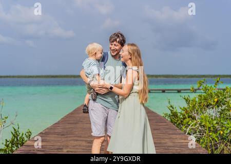 Maman, papa et leur bébé fils explorant la jetée en bois au-dessus des eaux turquoises du lac Bacalar, au Mexique. Concept de destination de voyage tropical paisible Banque D'Images