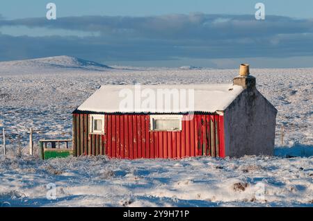 Un Shieling abandonné et délabré se trouve sur un paysage enneigé, son métal rouillé et son bois altéré racontant une histoire de temps et de négligence. Banque D'Images