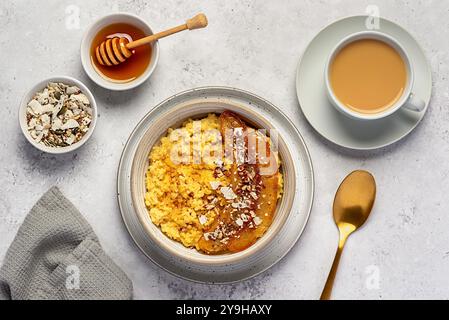 Photographie alimentaire de bouillie de millet avec banane caramélisée, noix de pécan, noix, flocons de noix de coco, chia, graines de lin, miel, thé au lait d'amande Banque D'Images