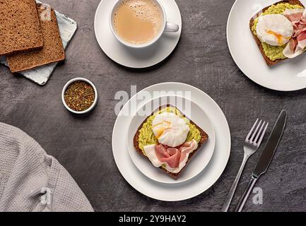 Photographie alimentaire du petit déjeuner nutritionnel, pain de seigle au levain avec de la purée d'avocat, prosciutto, bacon, oeuf poché bouilli, thé avec du lait Banque D'Images