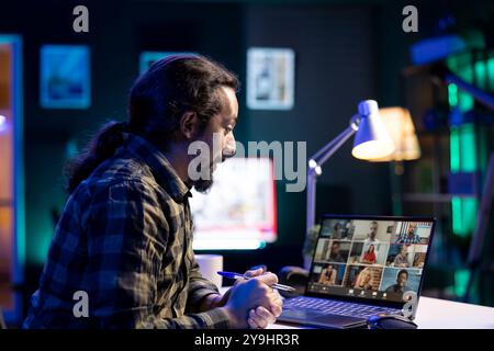 Un homme avec une barbe compare des documents avec un groupe de personnes de différents horizons dans une réunion virtuelle. Personne masculine assistant à la vidéoconférence sur son ordinateur portable numérique. Banque D'Images