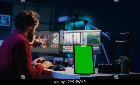 Tablette à écran vert sur le bureau dans le studio à côté de l'éditeur vidéo arrangeant les clips enregistrés dans l'ensemble transparent. Périphérique Chroma Key près du vidéaste assemblant les séquences enregistrées dans le projet fini Banque D'Images