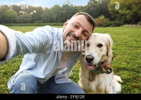 Homme souriant avec chien mignon Golden Retriever prenant selfie le jour du printemps Banque D'Images