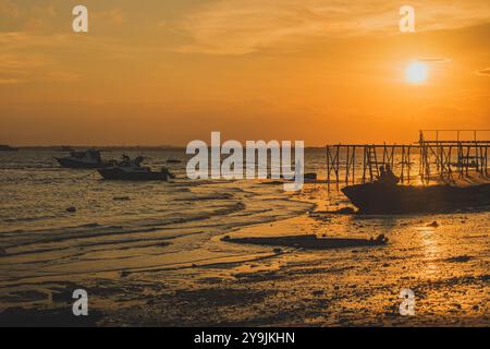 Des silhouettes de pêcheurs et de bateaux sont gravées contre un ciel de coucher de soleil vibrant. La lumière dorée se reflète sur le sable humide, créant une scène fascinante o Banque D'Images