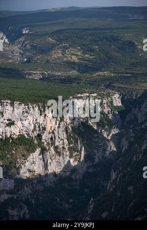 Falaises verdoyantes et grottes des gorges du Verdon en France, avec la lumière du soleil accentuant les formations géologiques et les ombres contrastées Banque D'Images