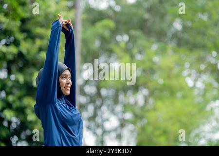 Femme musulmane mignonne asiatique portant des vêtements de sport et un hijab bleu s'exerçant et courant à l'extérieur au parc le matin. avec une sensation de fraîcheur. Banque D'Images