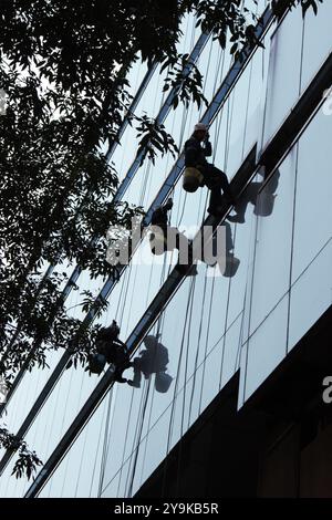 Trois nettoyeurs de vitres dans les hauteurs. Hommes nettoyant les fenêtres extérieures d'un bâtiment. Emplois risqués. Banque D'Images