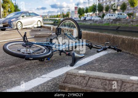 Un vélo se trouve sur le côté dans un parking à côté d'une rangée de voitures. La scène est située près d'une voie navigable et entourée de bâtiments et d'arbres. Banque D'Images