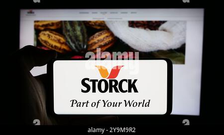 Dans cette illustration photo, une personne tient un téléphone portable avec le logo de la société allemande de confiserie August Storck KG en face de la page Web de l'entreprise. Banque D'Images