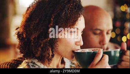 Noël, couple et se détendre à la maison avec du chocolat chaud, le confort et profiter de la saison des fêtes. Homme, femme et boire du coco dans le salon pour la chaleur, confortable Banque D'Images
