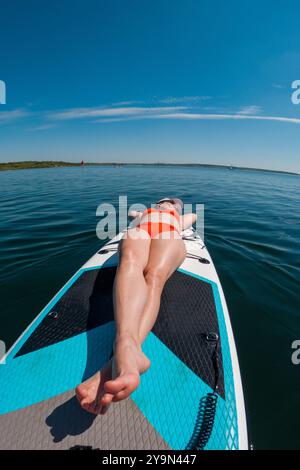 Femme se relaxant sur Paddleboard dans les eaux claires Banque D'Images