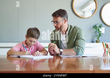 Père, fils et livres pour l'apprentissage à la maison, le soutien à l'éducation et l'amour pour l'enfant à la table de cuisine. Papa, garçon et soins pour enfant ou assistance avec Banque D'Images