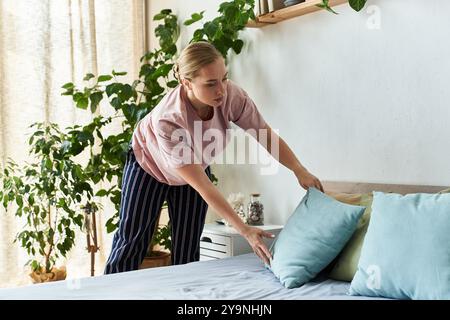 Une belle femme de grande taille dispose des oreillers sur son lit au milieu d'un jardin intérieur serein. Banque D'Images