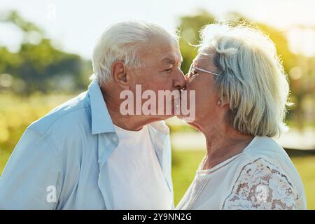 Amour, baiser et couple âgé dans le parc avec heureux, sourire et lier dans la nature ensemble. Homme senior, femme et romance dans le jardin avec confiance, soutien Banque D'Images