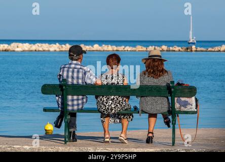 Trois personnes assises sur un banc en bois donnant sur la mer à travers le port dans la ville de Zakynthos dans la méditerranée ionienne par une journée ensoleillée Banque D'Images