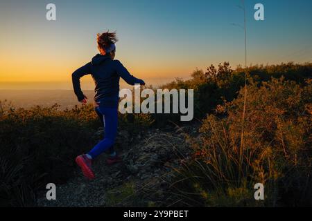 Un coureur s'entraîne dans les montagnes tandis que le soleil illumine le paysage. Banque D'Images