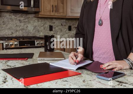 Gros plan d'une femme écrivant dans un cahier sur un comptoir de cuisine Banque D'Images