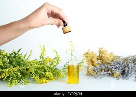 Femme goutte à goutte teinture de la pipette dans la bouteille et les herbes sur fond blanc, gros plan Banque D'Images