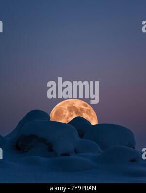 Pleine lune levant sur le paysage d'hiver avec des rochers couverts de neige. Banque D'Images