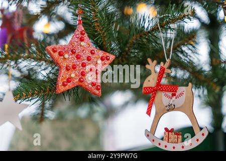 Étoiles rouges scintillantes et rennes en bois suspendus à un sapin de Noël artificiel Banque D'Images