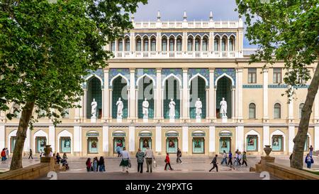 Bakou, Azerbaïdjan - 5 mai 2024 : Musée Nizami d'Azerbaïdjan, avec des statues bordant la façade. Le bâtiment est décoré avec des arches et des carreaux complexes. On peut voir des gens marcher près du bâtiment Banque D'Images
