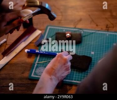 Main féminine travaillant sur le portefeuille en cuir dans son atelier Banque D'Images