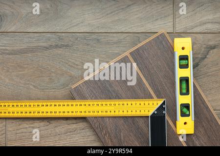 Règle d'angle, outil de niveau et pièces de revêtement de sol stratifié sur la surface en bois, vue de dessus Banque D'Images