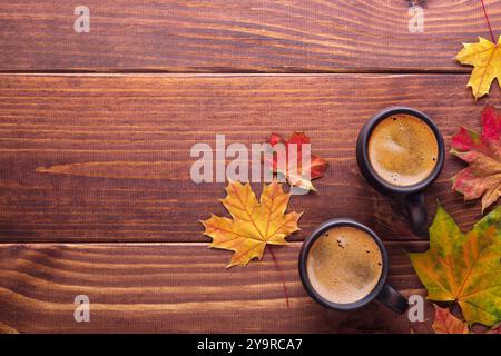 Feuilles d'érable d'automne multicolores et deux tasses d'argile brune avec du café noir sur une table en bois. Vue de dessus. Banque D'Images