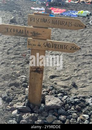 Panneau de signalisation en bois vers « Piscinas Naturais » et les monuments locaux sur une plage de sable noir à Mosteiros, île de São Miguel, Açores. Banque D'Images
