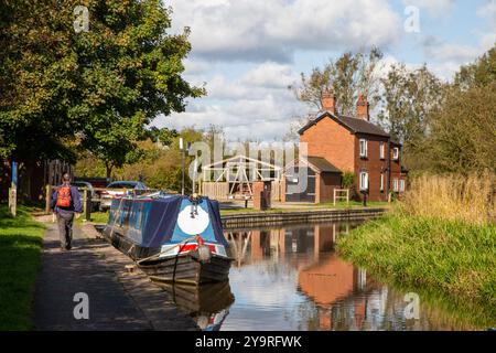 Homme marchant à dos le long du chemin de halage du canal de Caldon dans le Staffordshire approchant des services de Park Lane avec des bateaux étroits amarrés Banque D'Images