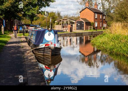 Homme marchant à dos le long du chemin de halage du canal de Caldon dans le Staffordshire approchant des services de Park Lane avec des bateaux étroits amarrés Banque D'Images