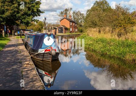 Homme marchant à dos le long du chemin de halage du canal de Caldon dans le Staffordshire approchant des services de Park Lane avec des bateaux étroits amarrés Banque D'Images