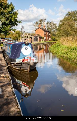 Homme marchant à dos le long du chemin de halage du canal de Caldon dans le Staffordshire approchant des services de Park Lane avec des bateaux étroits amarrés Banque D'Images