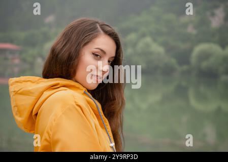 Une femme en veste jaune se tient devant un lac Banque D'Images