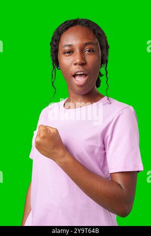 Une jeune femme avec des tresses exprime l'excitation avec un poing serré sur un fond vert vif Banque D'Images