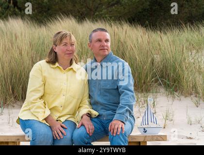 Couple adulte heureux dans l'amour assis sur le banc sur la plage. L'homme et la femme s'embrassent tendrement. Les relations familiales Banque D'Images