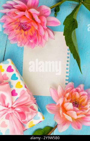 fond d'été. dahlias rose clair sur un fond bleu en bois, morceau de papier pour le texte. boîte avec un cadeau. Fête des mères, Fête des femmes, Festiva du printemps Banque D'Images