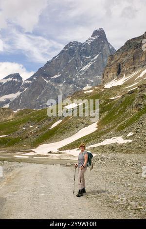 une femme randonneuse avec sac à dos et bâtons de randonnée s'arrête pour admirer l'impressionnant paysage montagneux des alpes sur le cervin sous un ciel bleu ensoleillé Banque D'Images