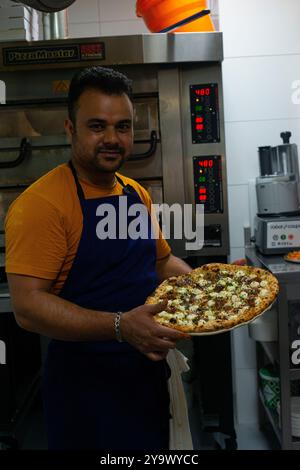 Assistant de cuisine montrant une pizza fraîchement sortie du four Banque D'Images