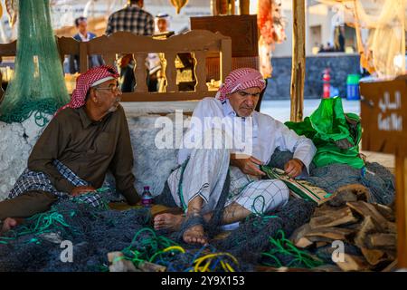 Doha, Qatar - 29 novembre 2023 : un homme arabe répare un filet de pêche pendant le festival des roulements à voile dans le village de Katara. Banque D'Images