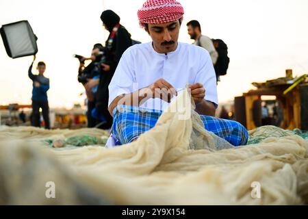 Doha, Qatar - 29 novembre 2023 : un homme arabe répare un filet de pêche pendant le festival des roulements à voile dans le village de Katara. Banque D'Images